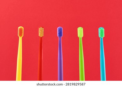 Colorful toothbrushes standing in a row, presenting vibrant colors on a red background. Emphasizing oral care and dental hygiene concepts