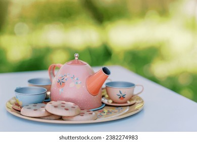 Colorful toy teapot with cups and cookies stands on a tray on a table in the garden for a tea party - Powered by Shutterstock