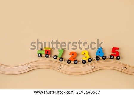Colorful toy train locomotive with numbers on wooden railway on beige background. Educational game. Learning to count through play.  Early education, peschool concept