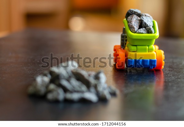 Colorful toy truck and a\
pile of rubble. A multi-colored toy carries rubble in a bucket.\
Transportation of building materials. Focus on a leaving truck in\
the background.