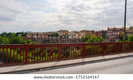 Colorful traditional houses built on the brick ramparts of the historic town of Rabastens, Southern France, overhanging the leafy embankments of the River Tarn, seen from the railing of a bridge