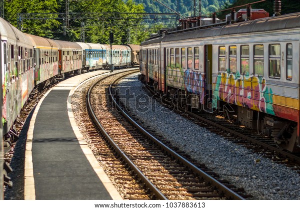 Colorful train\
wagons standing on railway tracks on a bright sunny summer morning.\
Empty track with concrete path turning on right between parked\
train compositions at a\
station.
