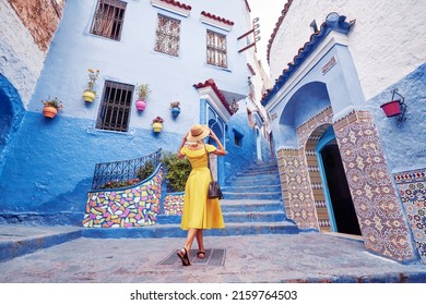 Colorful traveling by Morocco. Young woman in yellow dress walking in  medina of  blue city Chefchaouen.