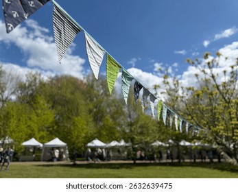 Colorful triangular bunting flags flutter in the breeze at an outdoor fair with tents and green trees in the background - Powered by Shutterstock - Get 15% off with code: PIKWIZARD15