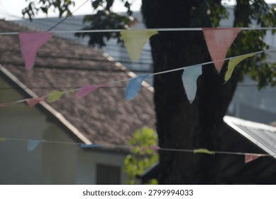 Colorful triangular bunting flags strung between trees in an outdoor setting with houses in the background