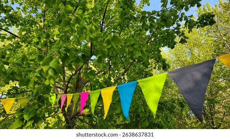 Colorful triangular bunting garland hanging among lush green tree branches. Festive outdoor decoration in nature, evoking celebration and summer joy. - Powered by Shutterstock - Get 15% off with code: PIKWIZARD15