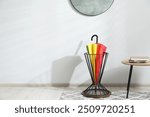 Colorful umbrella in stand near light wall. Space for text