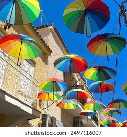 Colorful umbrellas hanging above a street in Greece, creating a vibrant canopy against a clear blue sky. The playful installation adds a splash of color and charm to the urban landscape. - Powered by Shutterstock