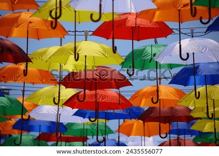 Colorful umbrellas and parasols, akin to open artworks, create a vibrant tapestry in the sky, turning rain and sunshine into a whimsical display of practical art.