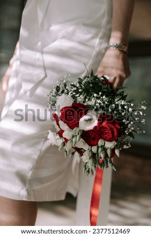 Colorful vertical wedding photograph showcasing a bride holding a bouquet in her lowered hand near her hip. The bride's face is not visible, adding an element of mystery and anticipation to the image.
