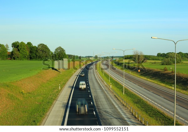 Colorful view\
from above on highway road with several cars. Green side fields and\
blue sky background.\
Sweden.
