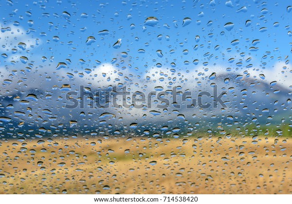 Colorful view of the mountains with fog, forest,\
blue sky and clouds through the window glass of the car covered by\
rain drops