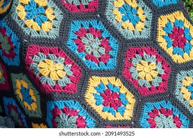 A colorful vintage craft crocheted blanket, multicolored; red, green, blue, and yellow color cotton wool. The textile pattern in the handmade afghan quilt is a flower with six sides and tidy stitches.