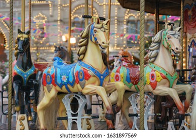 Colorful vintage merry-go-round wooden horses. Photography of the city amusement park in night. Downtown buildings as background. Concepts of fun and childhood.