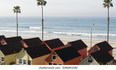 Colorful waterfront cottages in Oceanside, California USA. Multicolor bungalow huts by sea, beachfront lodging. Many vacation houses on beach, ocean waves and palm trees. Summer seascape on sunny day.