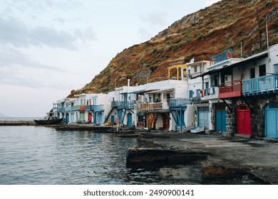 Colorful waterfront houses with balconies line a serene bay, set against a hillside, capturing the charm and beauty of a coastal village at dusk. - Powered by Shutterstock