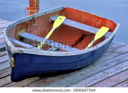 Colorful weathered rowboat painted red, white, and blue with yellow oars located on dock in coastal Maine.