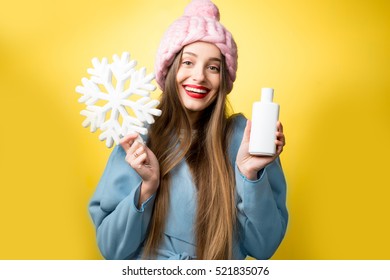 Colorful Winter Portrait Of A Beautiful Woman With Hair Conditioner Or Shampoo And Snowflake On The Yellow Background. Hair Care In Winter