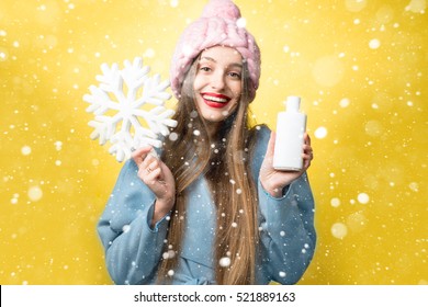 Colorful Winter Portrait Of A Beautiful Woman With Hair Conditioner Or Shampoo And Snowflake On The Yellow Background. Hair Care In Winter