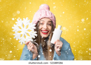 Colorful Winter Portrait Of A Beautiful Woman With Hair Conditioner Or Shampoo And Snowflake On The Yellow Background. Hair Care In Winter