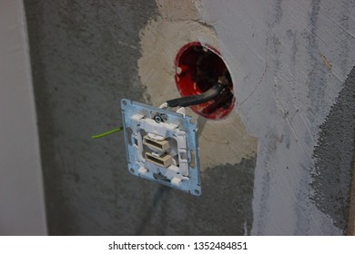 Colorful Wires Sticking Out Of The Wall, Repair The Apartment, House Or Office. Electrical Wiring. Light Bulb And Switch On The Background Of Gray Concrete Wall.