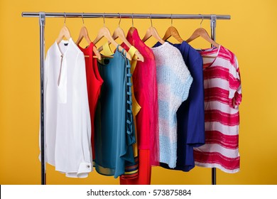 Colorful Womens Clothes On Hangers On Rack On Orange Background.