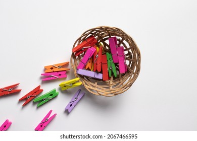 Colorful wooden clamps in wicker basket against white paper background. Flat lay. Top view.