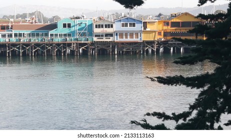 Colorful wooden houses on piles, pillars or pylons, ocean sea water, historic Old Fisherman's Wharf, Monterey bay or harbor, California coast USA. Tourist beachfront promenade, waterfront boardwalk.
