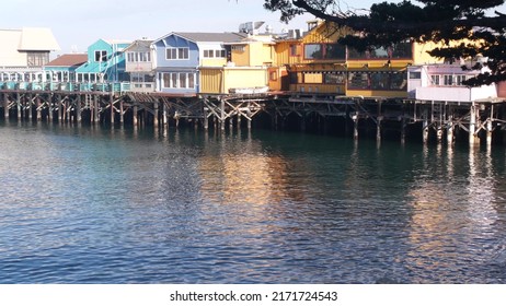 Colorful wooden houses on piles, pillars or pylons, ocean sea water, historic Old Fisherman's Wharf, Monterey bay or harbor, California coast USA. Tourist beachfront promenade, waterfront boardwalk.