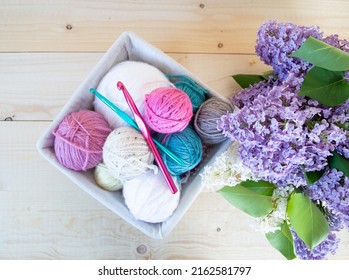 colorful woolen balls with crochet hook in a basket on wooden ground with purple lilac flower spring