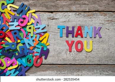 The colorful words "THANK YOU" made with wooden letters next to a pile of other letters over old wooden board.