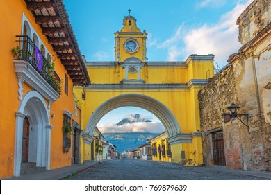 The colorful yellow arch of Antigua city at sunrise with the active Agua volcano in the background, Guatemala.