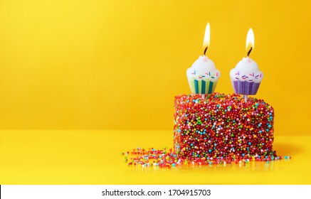 Colorfull birthday cake with red sprinkles and two candles on a yellow background with copyspace. Festive background, birthday.