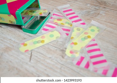 Colorfull Plasters Or Band Aid. A Plaster Box And Plasters Laying On A Light Wooden Table Detailed Close Up Taken From Above