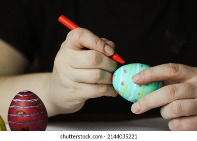 Coloring Easter eggs with pastel red wax crayon. Green Easter egg in women's hands before dyeing colors at home. Easter egg festival. Artistic work, handmade, DIY. People preparing for Easter in April