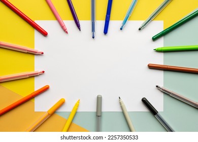 
				coloring markers around an empty sheet of white paper on a colorful child's desk. Background for drawing and coloring with blank space