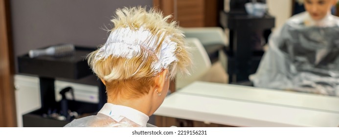 Coloring White Hair With Hair Dye Of The Young Caucasian Blonde Woman Sitting At A Hair Salon, Close Up