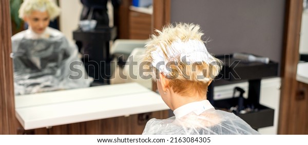 Coloring white hair\
with hair dye of the young caucasian blonde woman sitting at a hair\
salon, close up