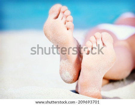 Colorized vintage photo of woman's feet on the white sand near the sea.