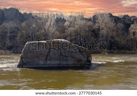 A colossal boulder, shaped uncannily like an elephant, stands steadfast in the flowing waters of the Southern Bug river under a dramatic sunset sky