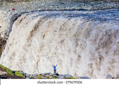 Colossal Roaring Waterfall Dettifoss. Elderly Woman Admires The Picturesque Spectacle. Huge Masses Of Water Cascading Into The Abyss. Iceland, Jokulsargljufur National Park