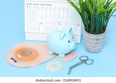 A colostomy bag, piggy bank, medical scissors, a flower in a pot and a calendar 2022 lie on a light blue background, side view. Colon cancer concept, surgery, business, cost of treatment and operation