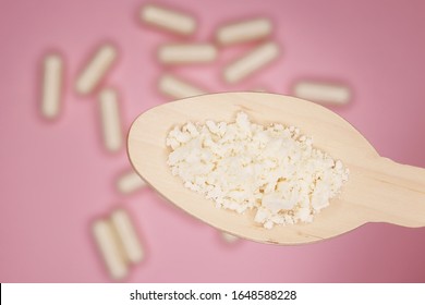 Colostrum powder, in a wooden spoon, on a pink background