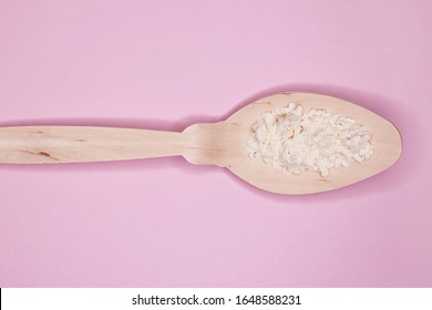 Colostrum powder, in a wooden spoon, on a pink background