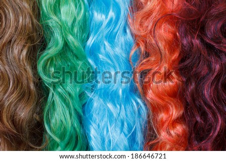 Coloured wigs with long wavy fake hair hanging next to each other.