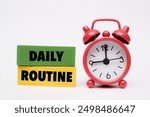 A coloured wooden block with text "DAILY ROUTINE" on it next to red alarm clock