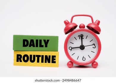 A coloured wooden block with text "DAILY ROUTINE" on it next to red alarm clock - Powered by Shutterstock