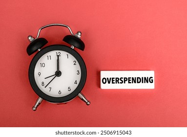 A coloured wooden block with text OVERSPENDING next to black alarm clock - Powered by Shutterstock