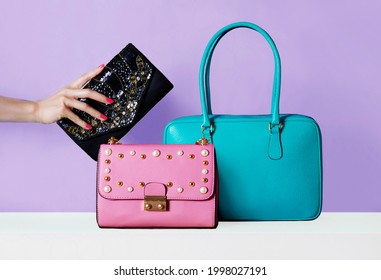 Farbige Taschen, violetter Hintergrund. Weibliche Hand mit roten, handgemachten Nägeln, die eine Brieftasche halten.