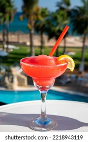 Colourful Frozen Pink Strawberry Daiquiri Cocktail Drink Served In Glass At Outdoor Cafe Overlooking Blue Pool, Sea And Palm Trees, Relax And Holidays At Sea